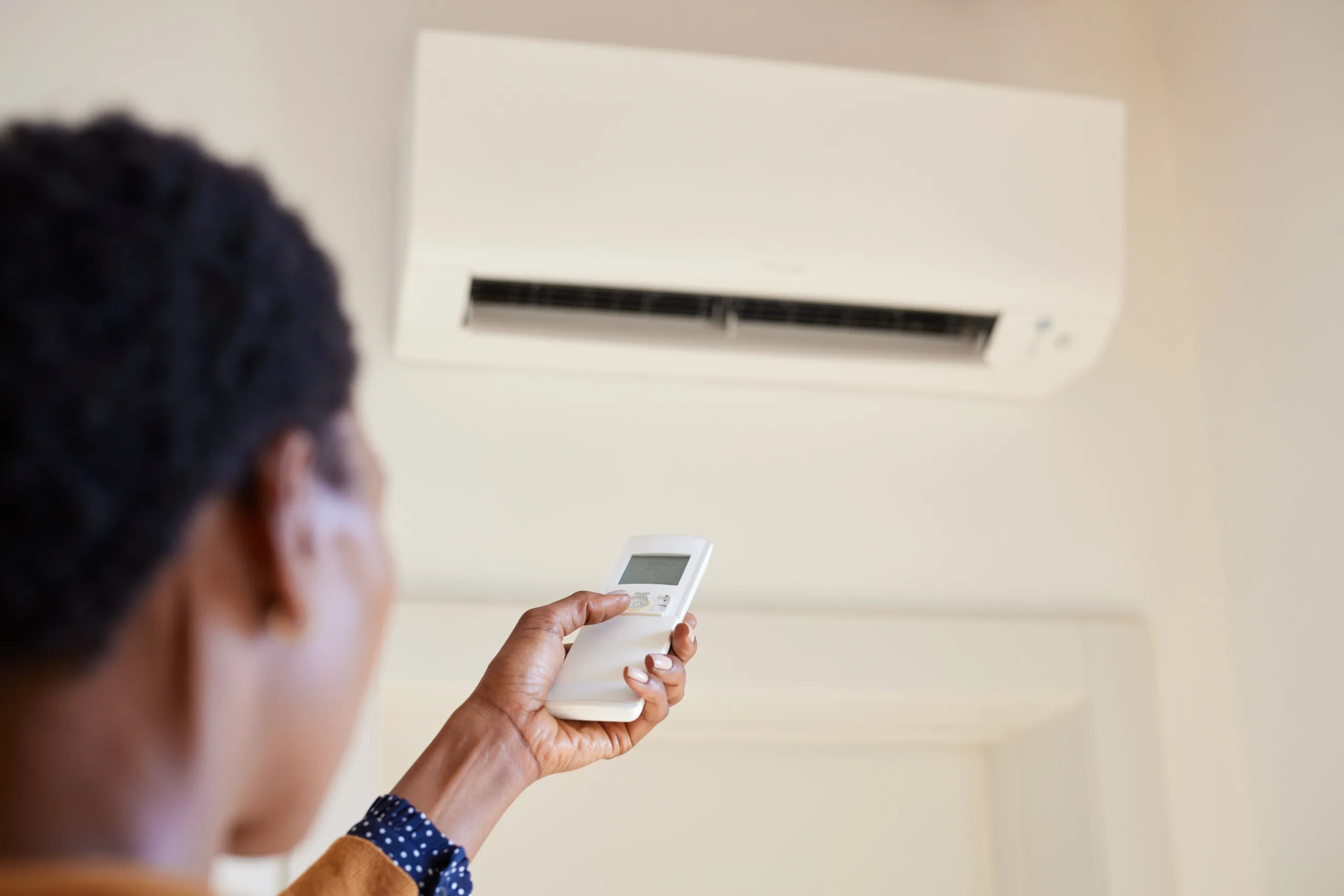 woman turning on wall mounted ac unit with remote